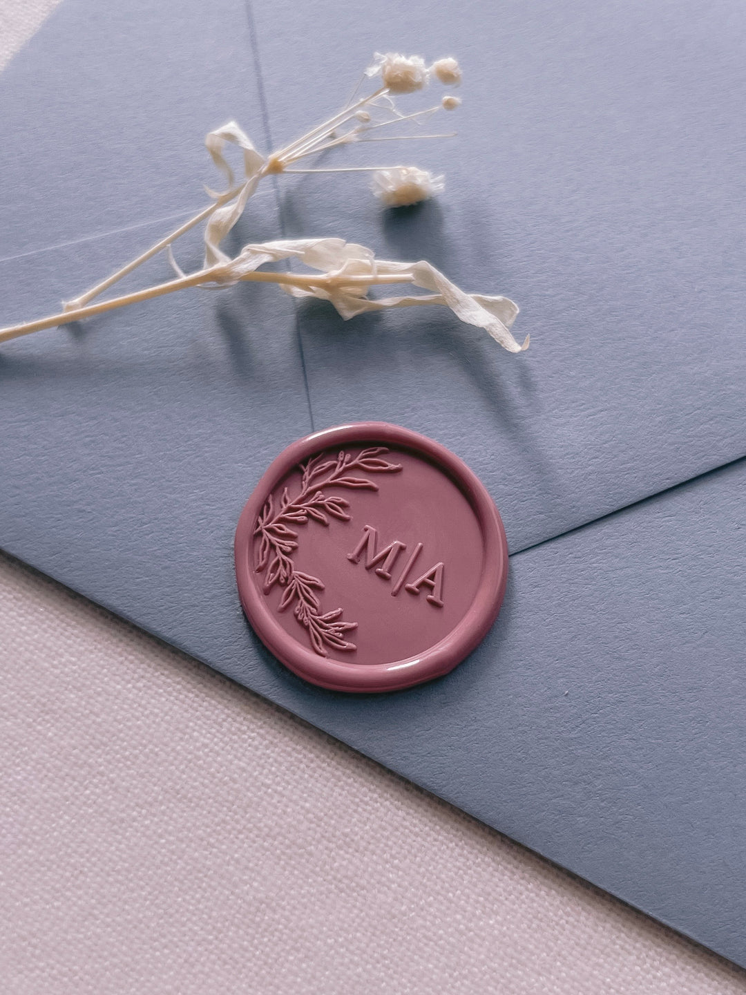 rose colored botanical custom initials wax seal on a dusty blue envelope 