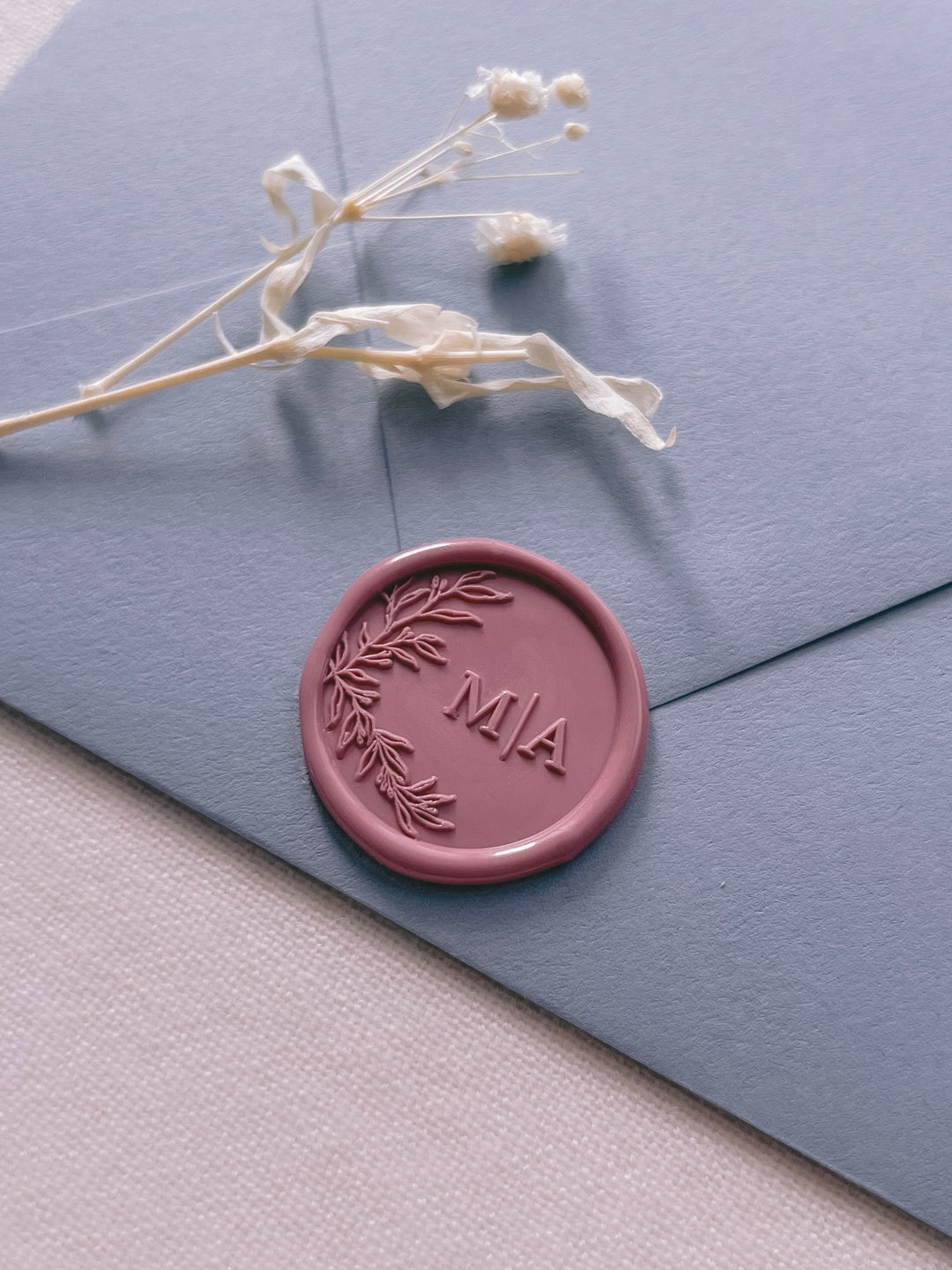 Rose pink personalized initials wax seal featuring a custom botanical monogram on a dusty blue envelope
