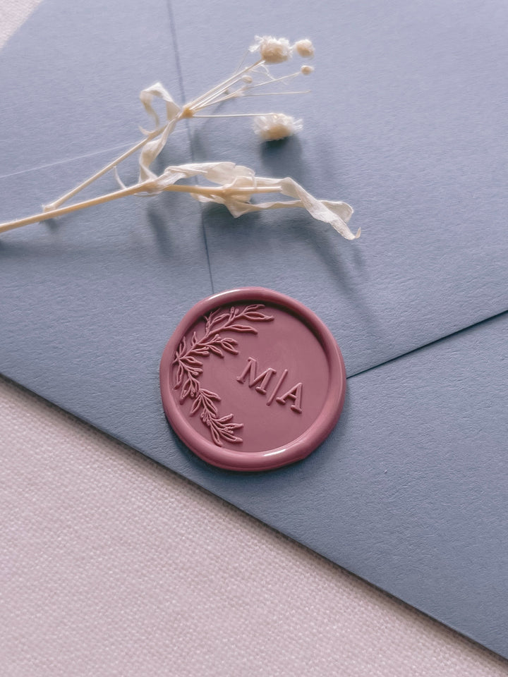 Rose pink personalized initials wax seal featuring a custom botanical monogram on a dusty blue envelope