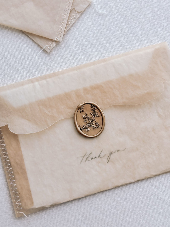 Gold botanical vine oval wax seal on a brown vellum envelope with handwritten "thank you" note inside.