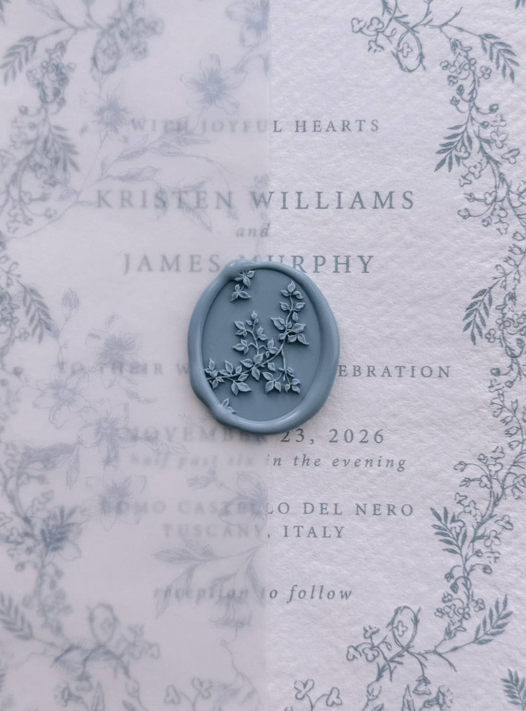 Dusty blue botanical vine wax seal on a vellum overlay, layered over a hand-illustrated floral wedding invitation card.