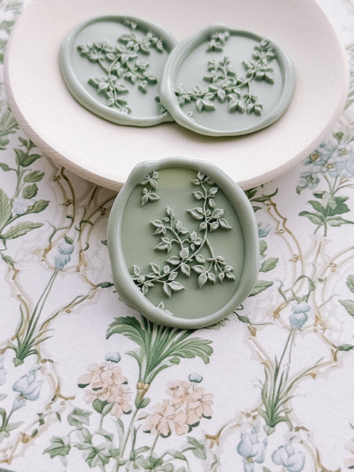 Sage green botanical vine wax seals displayed on a ceramic dish, set against a vintage floral backdrop.