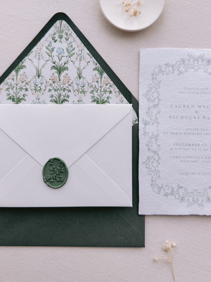 Dark green botanical vine oval wax seal on a white wedding invitation envelope, paired with a floral-lined envelope and ornate wedding invitation suite.