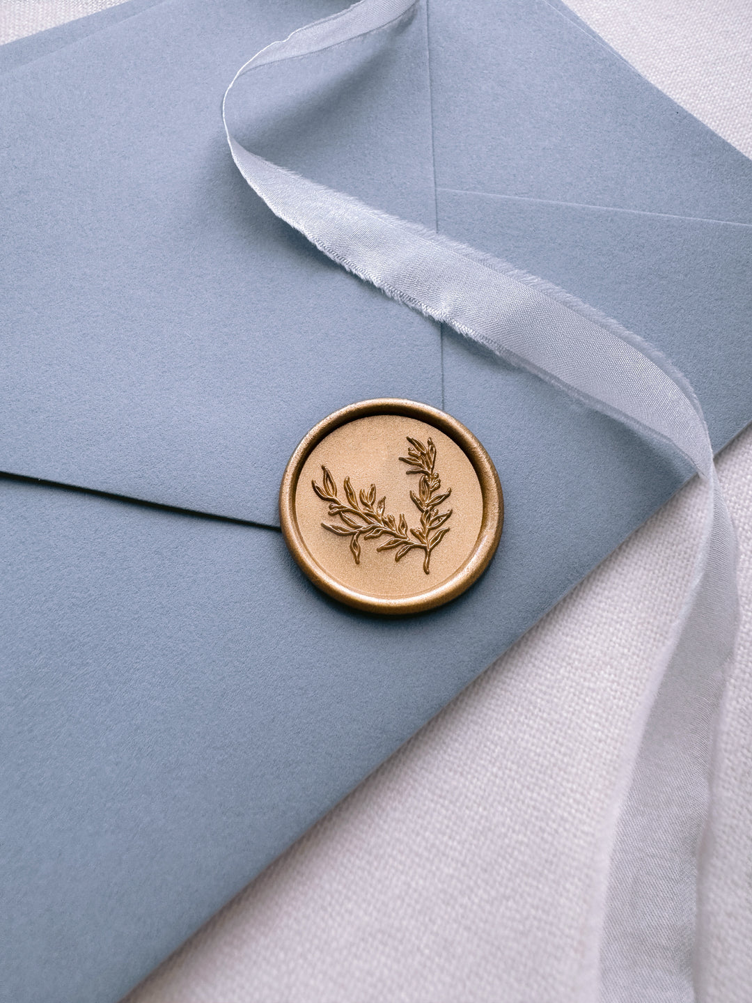 gold botanical wax seal on a dusty blue envelope