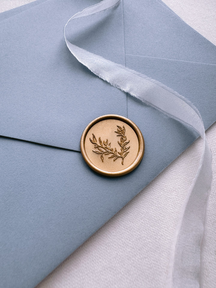 gold botanical wax seal on a dusty blue envelope