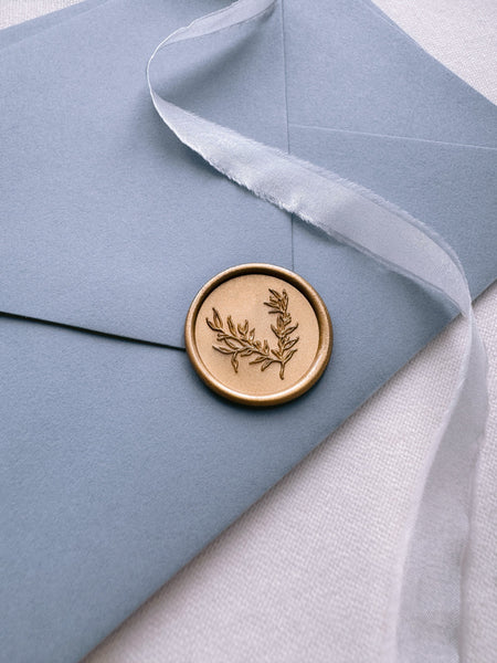 Delicate botanical gold wax seal on a dusty blue envelope