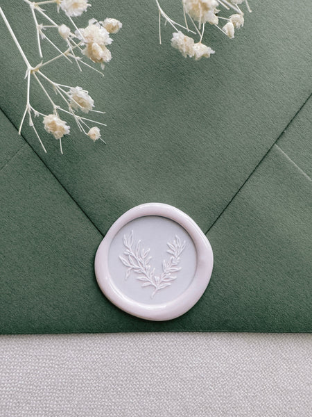 Light pink wax seal with a botanical print on a olive green envelope