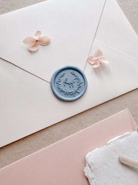 dusty blue botanical wreath wax seal with personalized initials on a light pink envelope