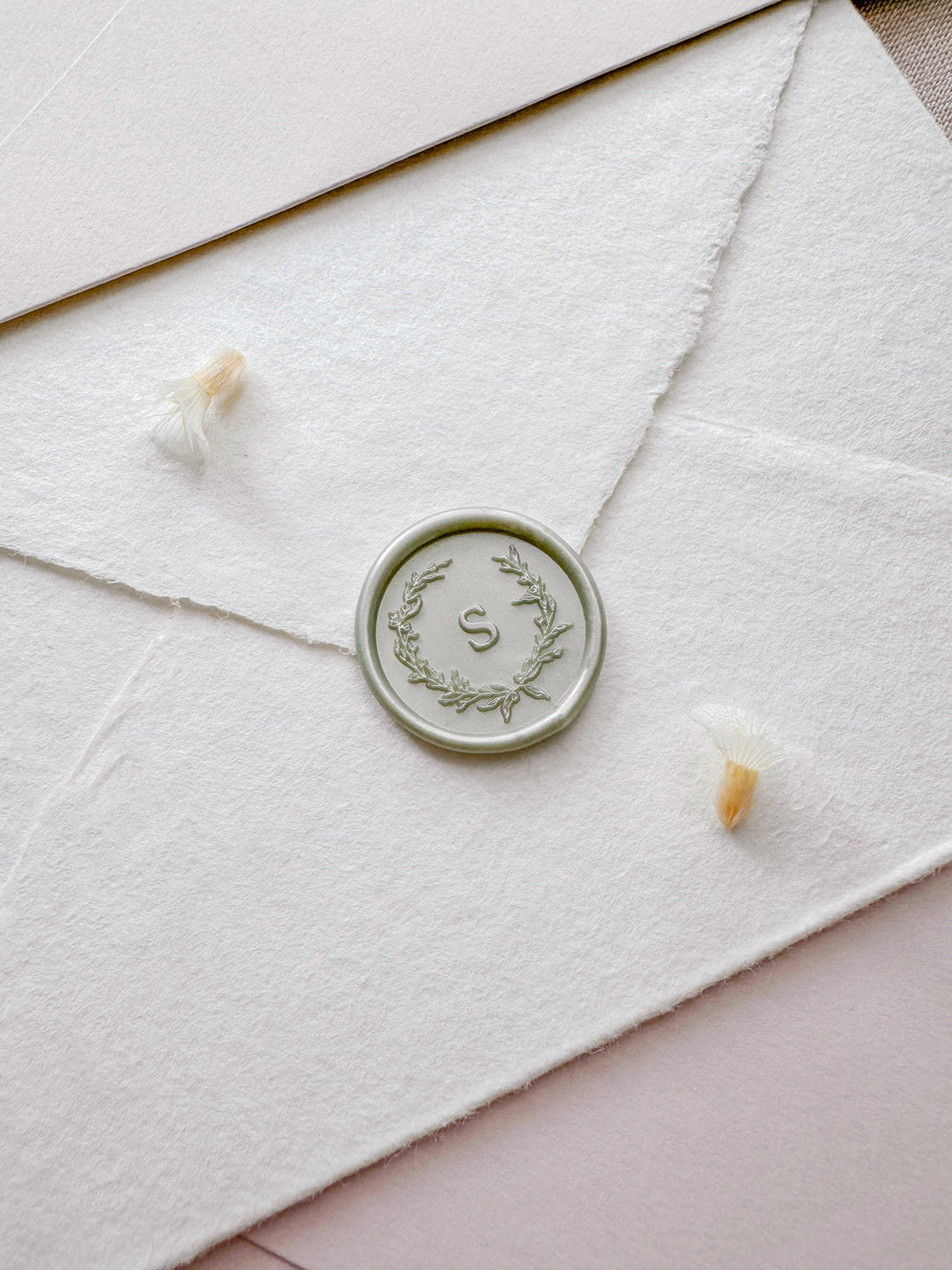 light metallic sage green wax seal featuring a personalized initial with a botanical wreath design