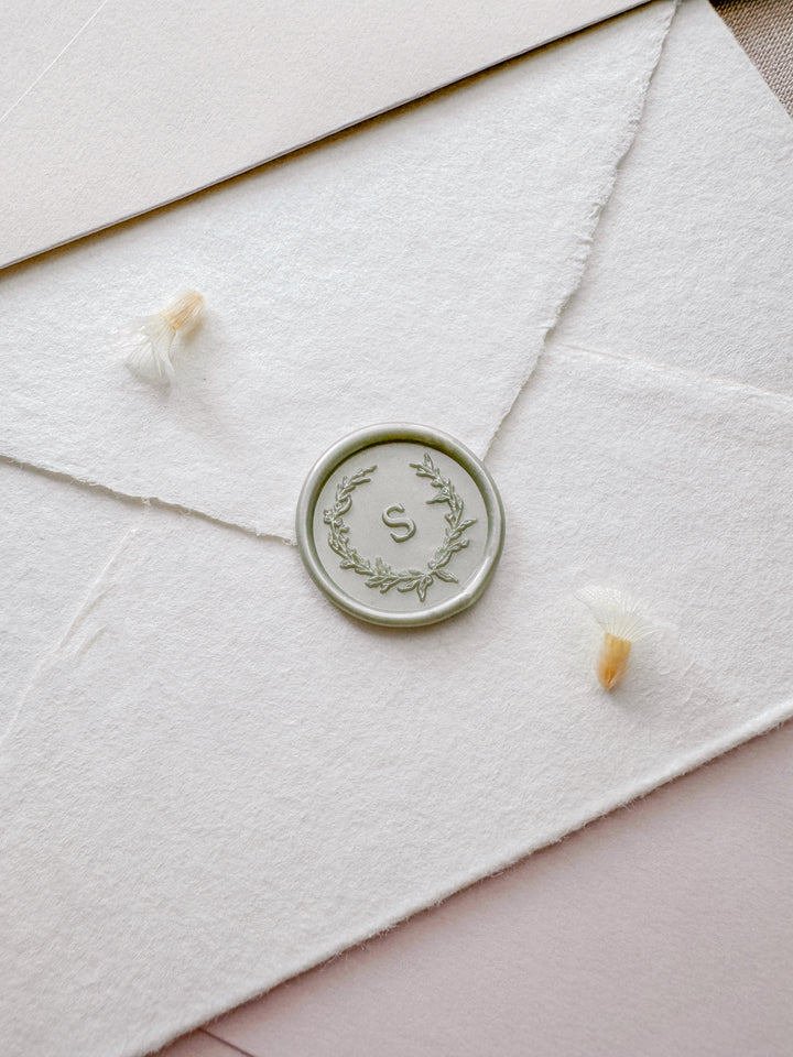 light metallic sage green wax seal featuring a personalized initial with a botanical wreath design