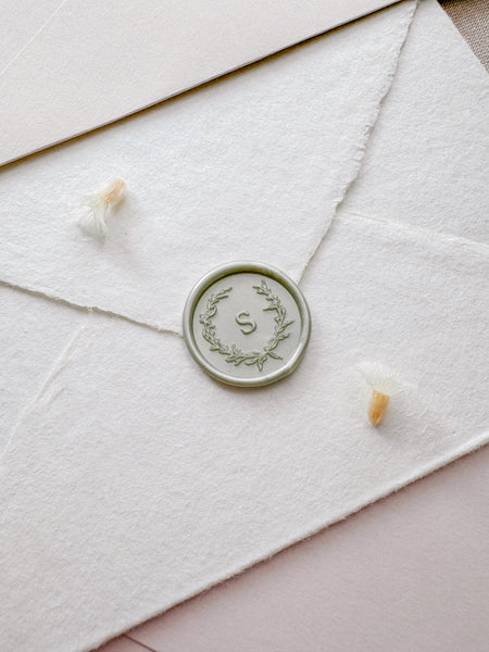 light metallic sage green wax seal featuring a personalized initial with a botanical wreath design 
