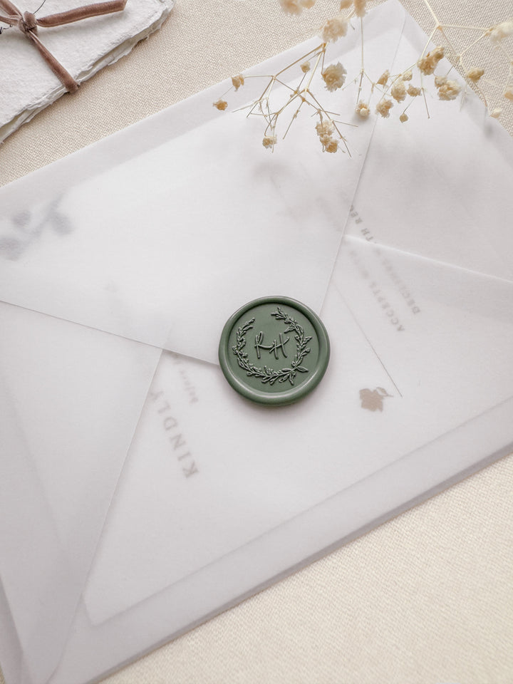 sage green botanical wreath monogram wax seal on a vellum wedding invitation envelope