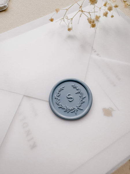 dusty blue custom initial wax seal with a leaf wreath design on a vellum envelope