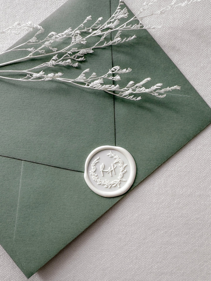 white custom initial botanical wreath design wax seal on an olive green envelope