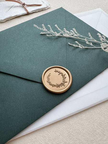 Gold wax seal featuring a delicate botanical wreath design on a dark green envelope