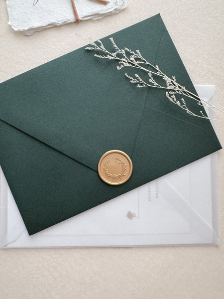 Gold wax seal featuring a delicate botanical wreath design on a dark green envelope