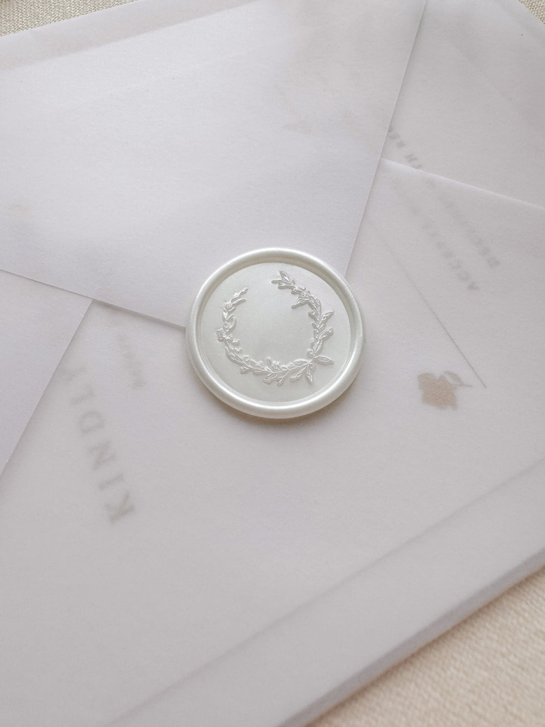 Pearl white wax seal featuring a delicate botanical wreath design on a vellum wedding invitation envelope