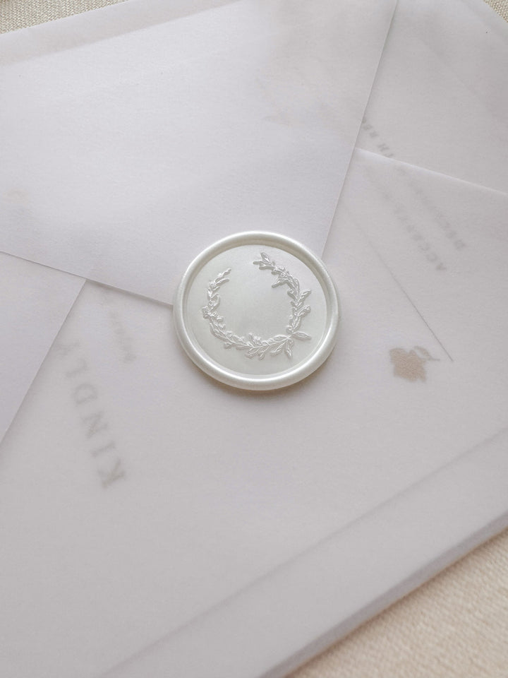 Pearl white wax seal featuring a delicate botanical wreath design on a vellum wedding invitation envelope