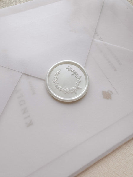 Pearl white wax seal featuring a delicate botanical wreath design on a vellum wedding invitation envelope