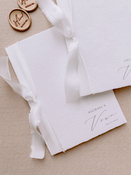 A set of two His and Her personalised handmade paper vow books in calligraphy script with soft white colored silk ribbon styled with gold wax seals