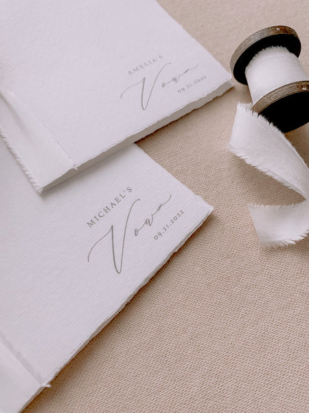 A set of two His and Her personalised handmade paper vow books in calligraphy script with soft white colored silk ribbon styled with a spool of soft white silk ribbon