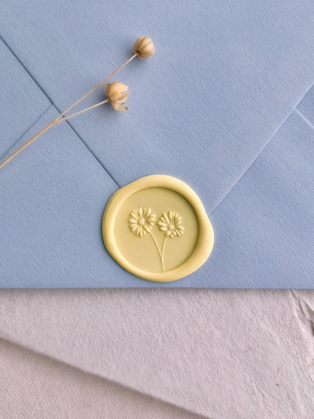 pastel butter yellow colored 3D daisies design wax seal on a light blue envelope