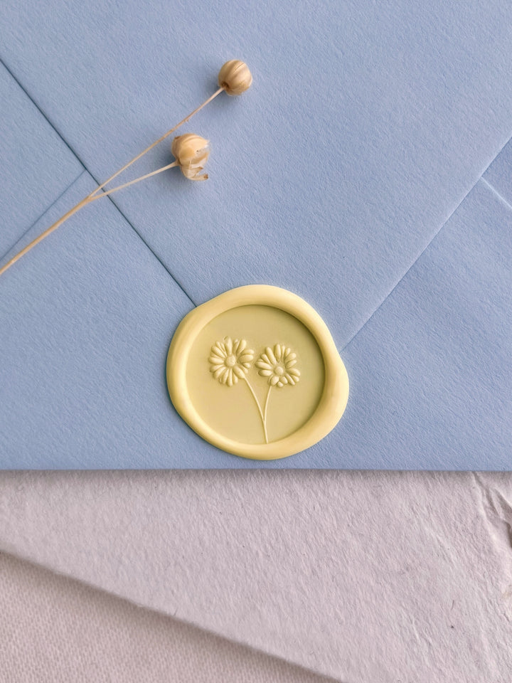 pastel butter yellow colored 3D daisies design wax seal on a light blue envelope