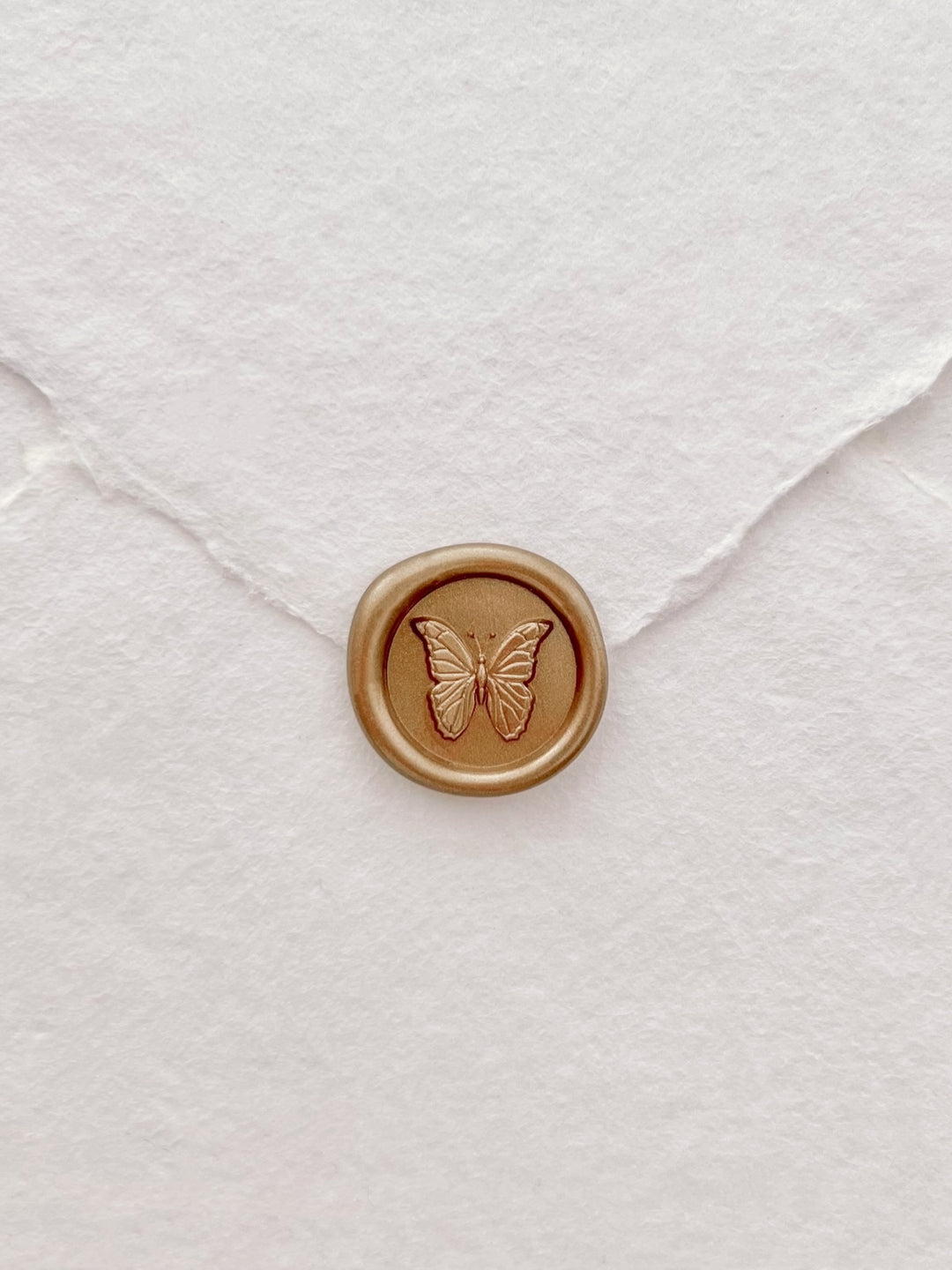 gold 3D butterfly mini wax seal on a flap of a white deckle-edge handmade paper wedding envelope