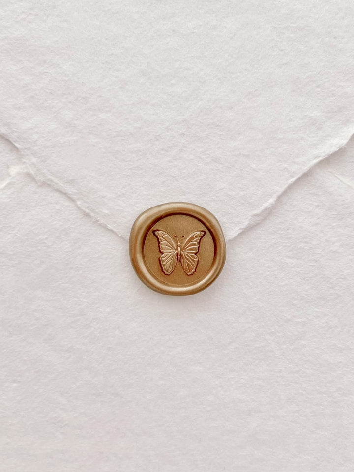 gold 3D butterfly mini wax seal on a flap of a white deckle-edge handmade paper wedding envelope