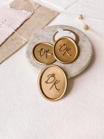 Calligraphy monogram oval custom wax seals in gold styled with a small gray stone dish, handmade paper and a dried floral branch