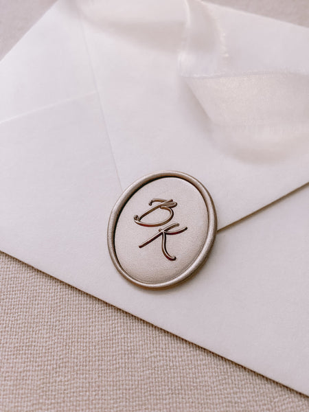 Calligraphy monogram oval custom wax seal in mocha on white paper envelope styled with a strand of white silk ribbon