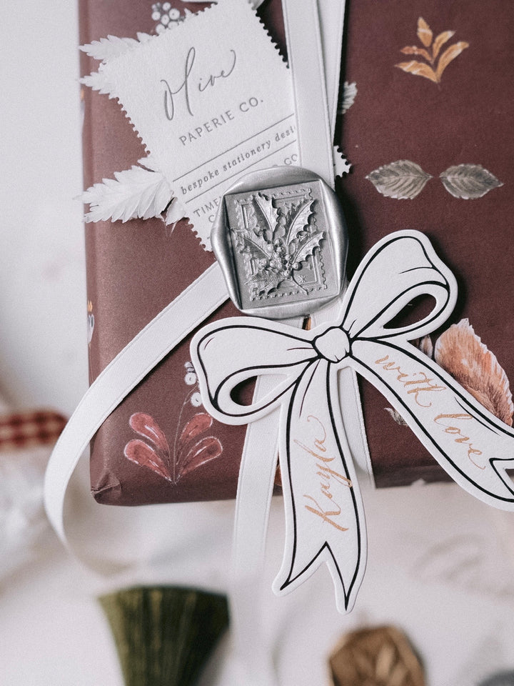 A close-up image of a wrapped gift box with a bow, featuring a wax seal and a decorative ribbon.