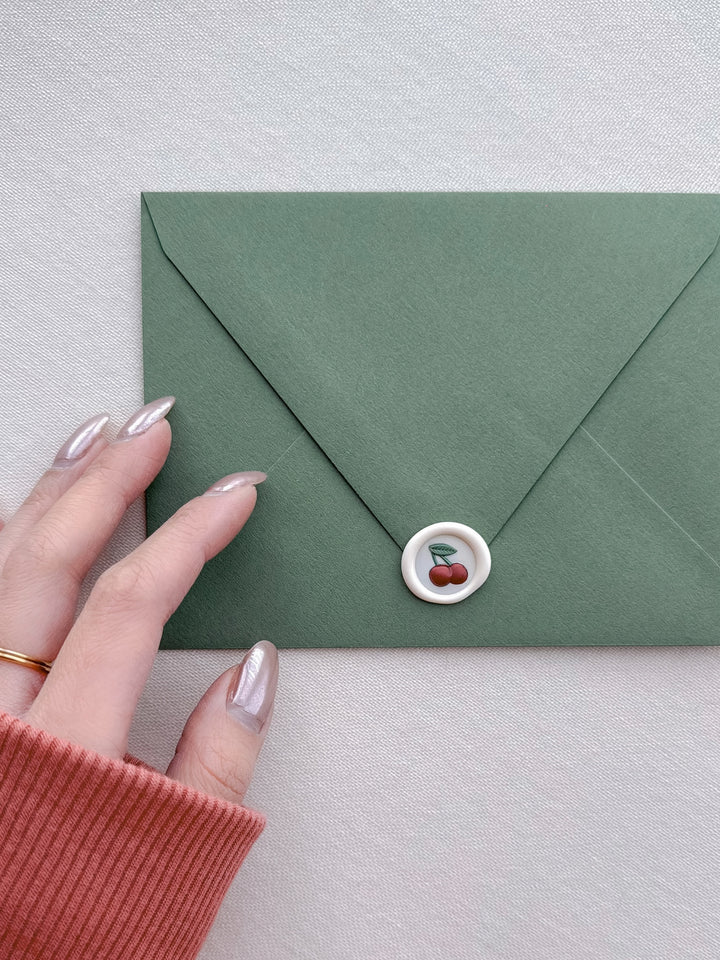 mini cherry emoji wax seal on a green envelope