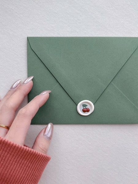 mini cherry emoji wax seal on a green envelope