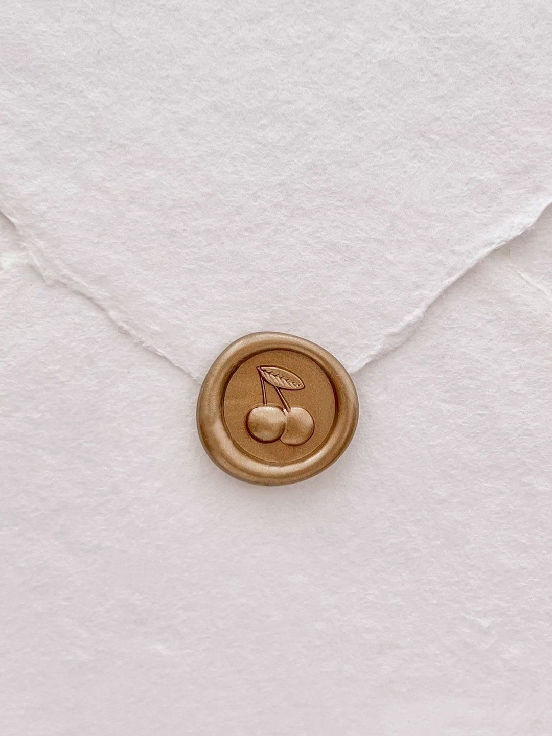 Gold mini 3D cherry wax seal on a white deckled edge handmade paper envelope 