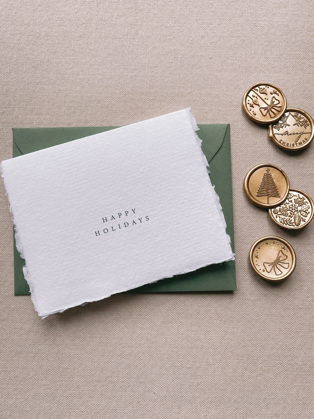 Happy holidays handmade Christmas cards with olive green envelope with assorted designs of christmas ornaments, merry christmas, christmas tree, winter garden and ribbon bow Christmas wax seals in gold beside the card