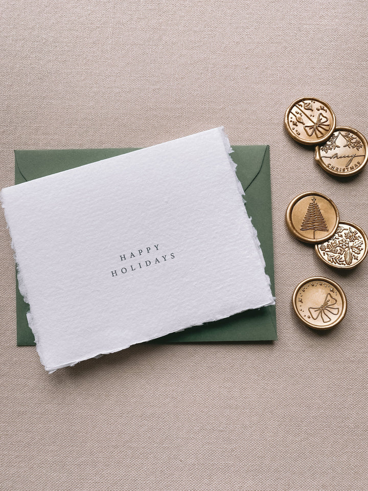 Happy holidays handmade Christmas cards with olive green envelope with assorted designs of christmas ornaments, merry christmas, christmas tree, winter garden and ribbon bow Christmas wax seals in gold beside the card