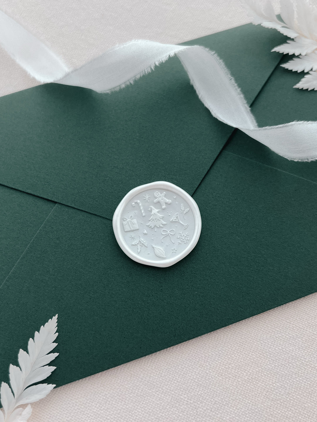 Pearl white Christmas wax seal featuring a design of festive icons such as gingerbread man, candy cane, snowflake, Christmas tree and more