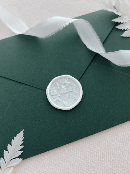 pearl white Christmas wax seal with festive icons and symbols like Christmas tree, gingerbread man, snowflake, holly and candy cane on a green envelope