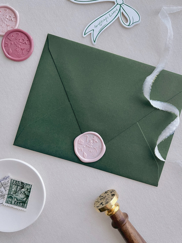 pink Christmas wax seal with festive symbols such as Christmas tree, gingerbread man, snowflake, holly and candy cane on an olive green envelope