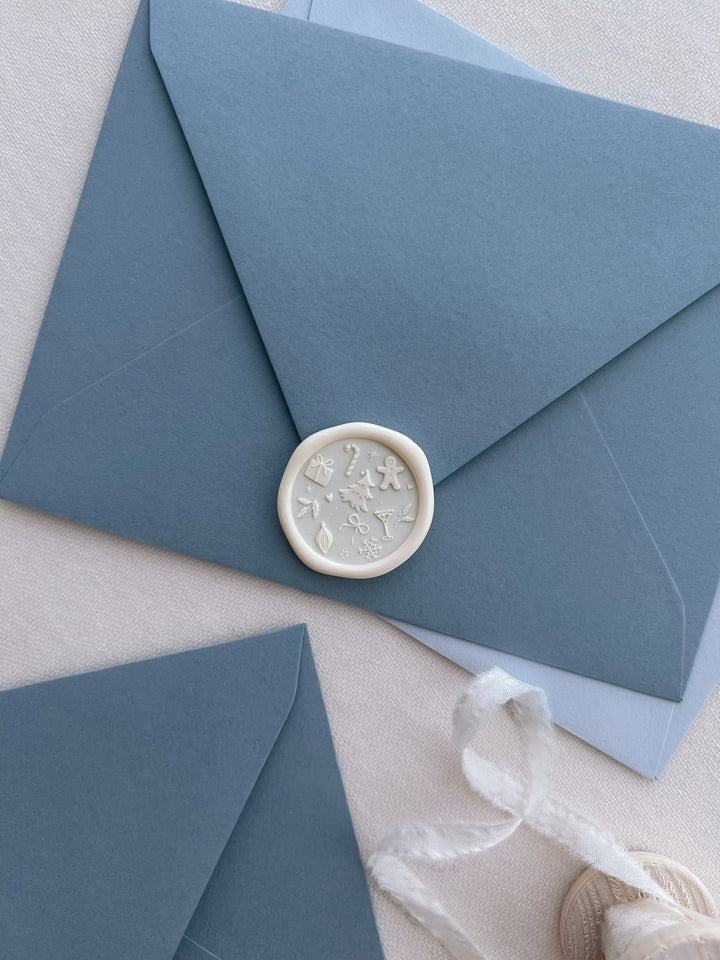 white Christmas envelope seal with festive icons and symbols such as Christmas tree, gingerbread man, snowflake, holly and candy cane, on a dusty blue envelope