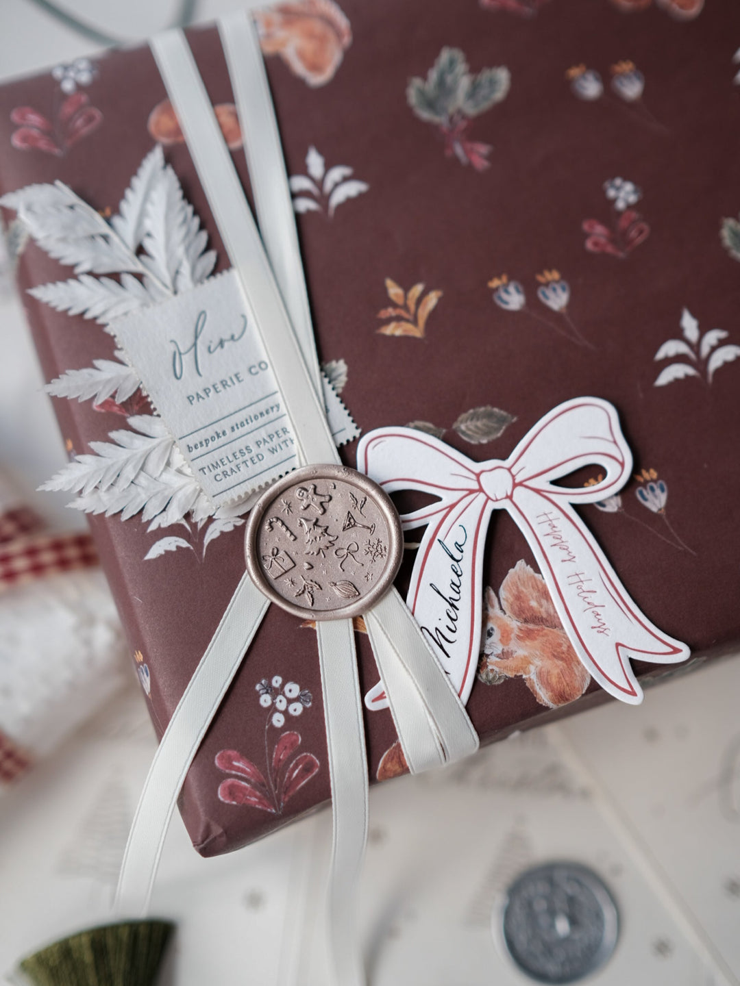 Light bronze festive wax seal with Christmas icons and symbols like Christmas tree, gingerbread man, snowflake, holly and candy cane on a personalised gift tag and a wrapped gift