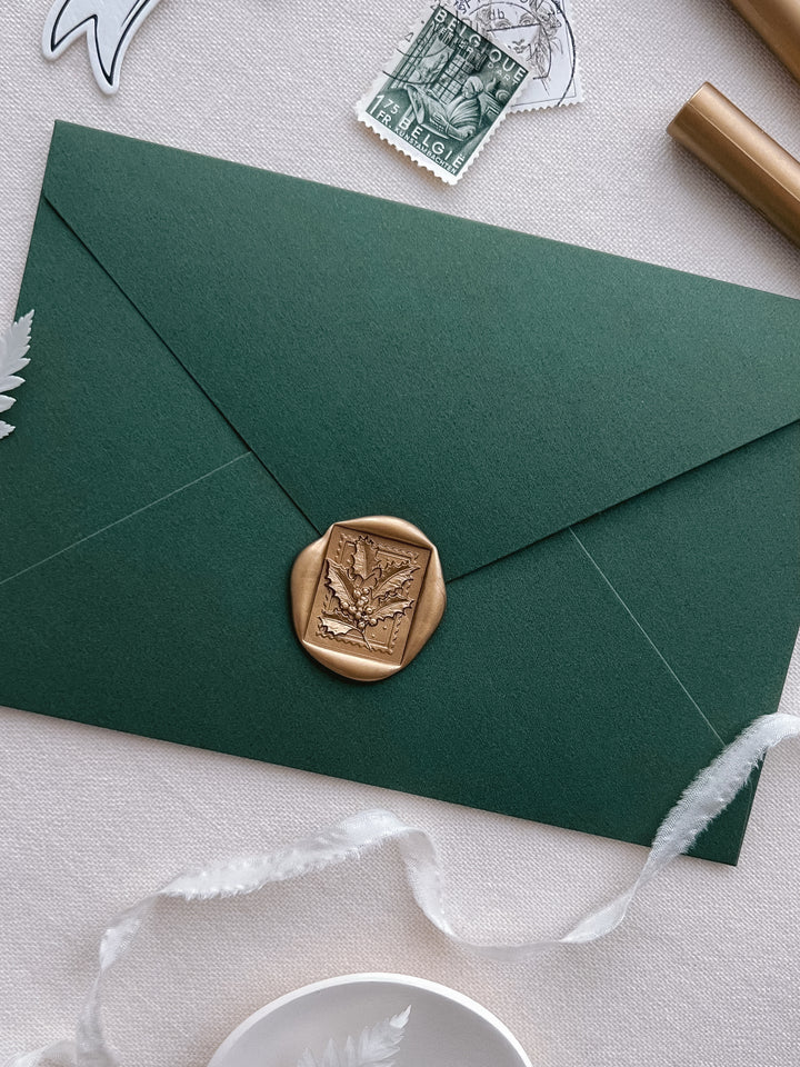gold Christmas holly leaf rectangular wax stamp on a dark green Christmas card envelope