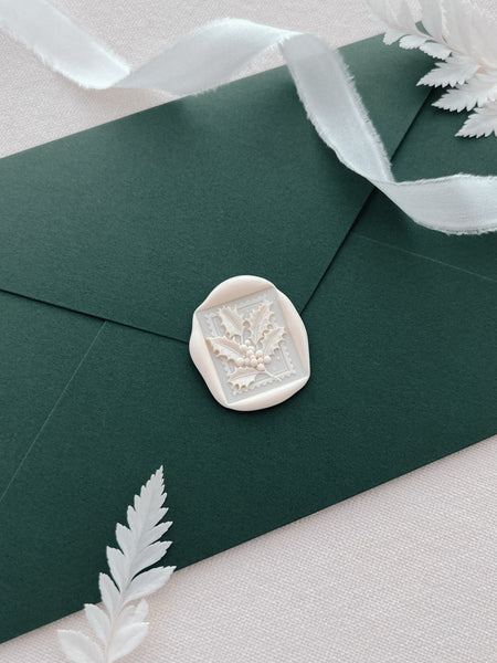 white Christmas holly wax seal on a dark green Christmas envelope