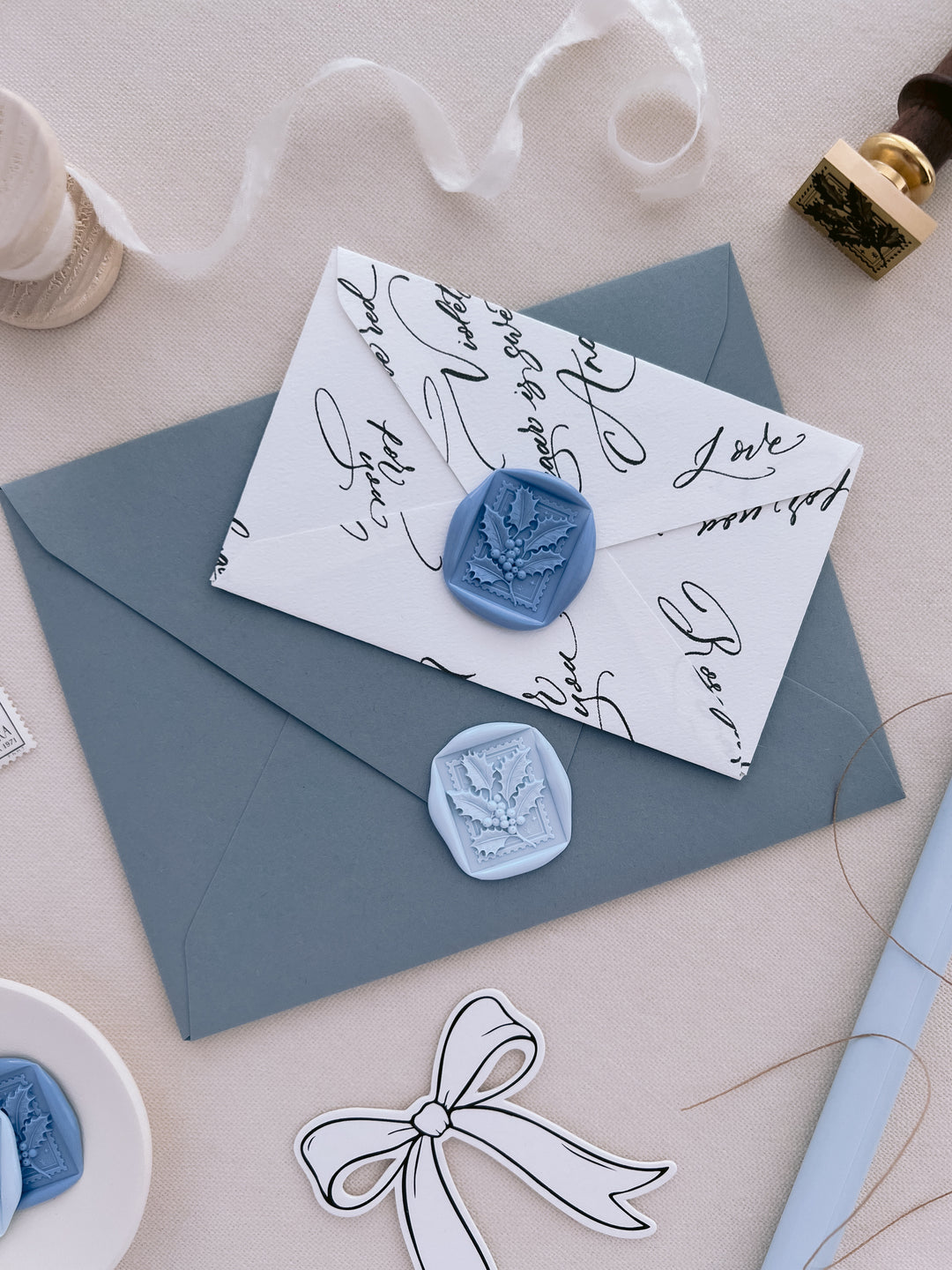blue and light blue Christmas holly leaf design wax seals on dusty blue and white envelopes styled with festive props