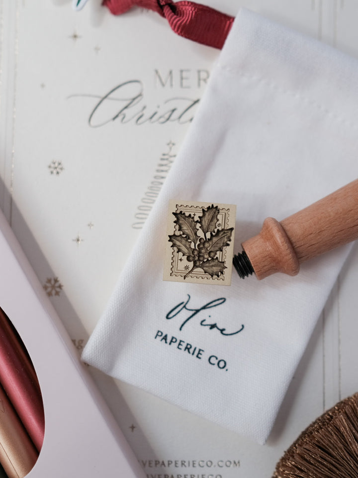 Festive Christmas holly wax seal stamp with a wooden handle on a storage pouch