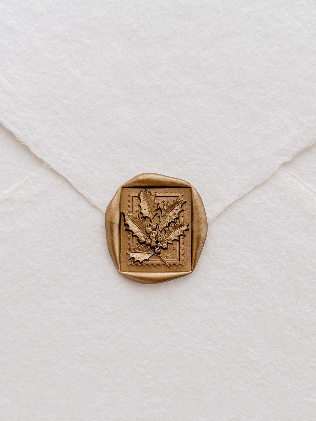 Gold Christmas holly and berries square wax seal on a white handmade paper envelope
