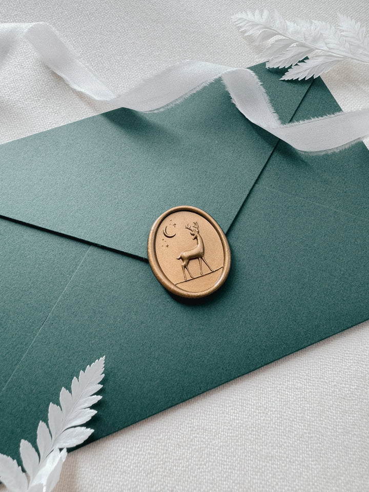 Gold 3D reindeer oval wax seal on a dark green envelope on a white background