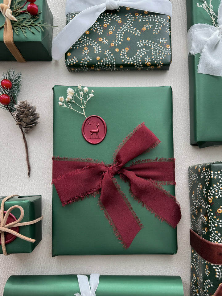 Dark metallic red 3D reindeer oval wax seal on a dark green Christmas gift surrounding with other Christmas gifts