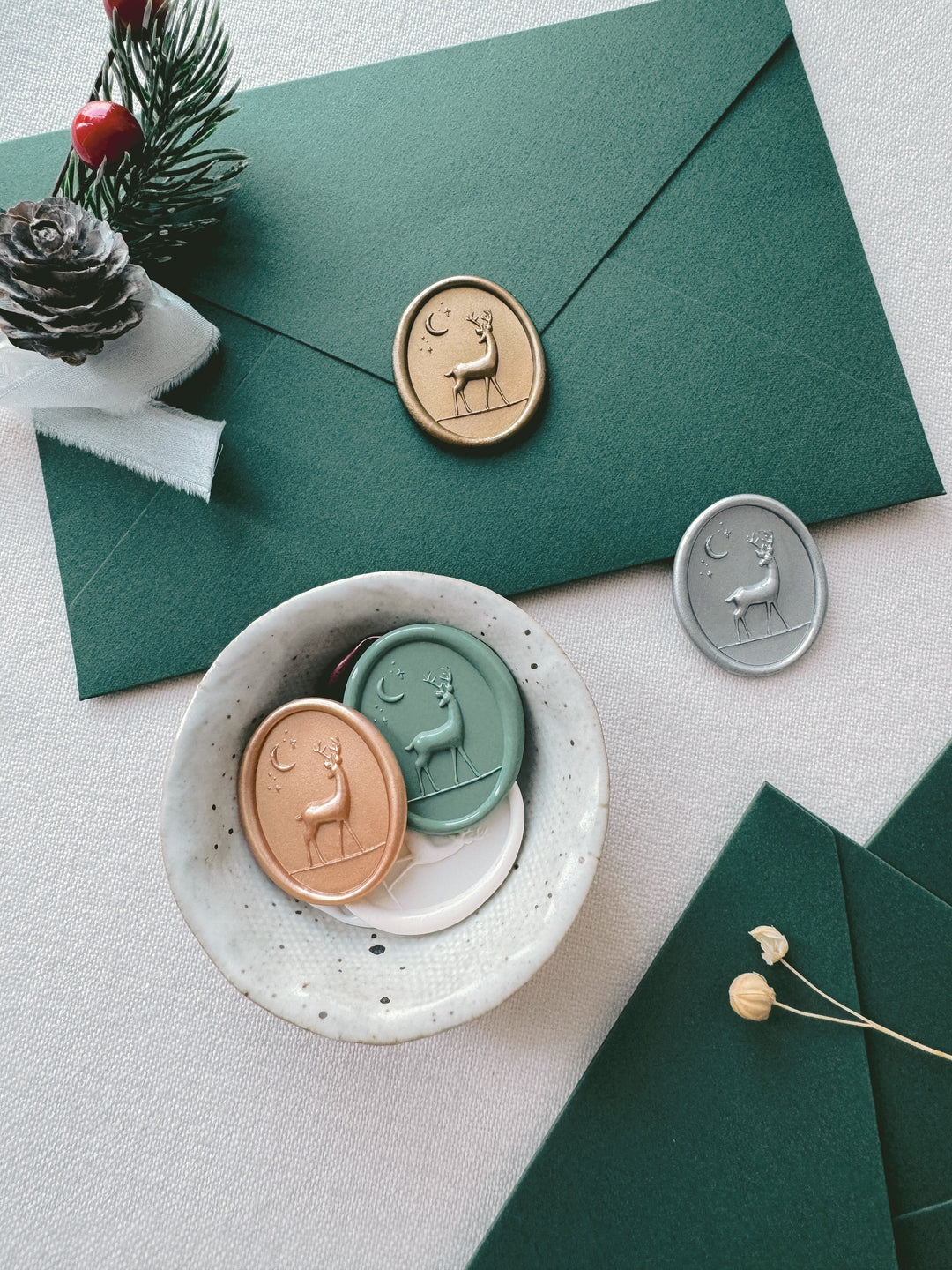 3D reindeer oval wax seals in various festive wax colors on a dark green envelope and in a small ceramic dish 